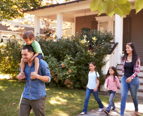 Gebäudeversicherung und Gebäudehaftpflicht: Eine Junge Familie mit 3 Kindern, der Sohn auf den Schultern des Vaters laufen glücklich aus dem Haus raus.